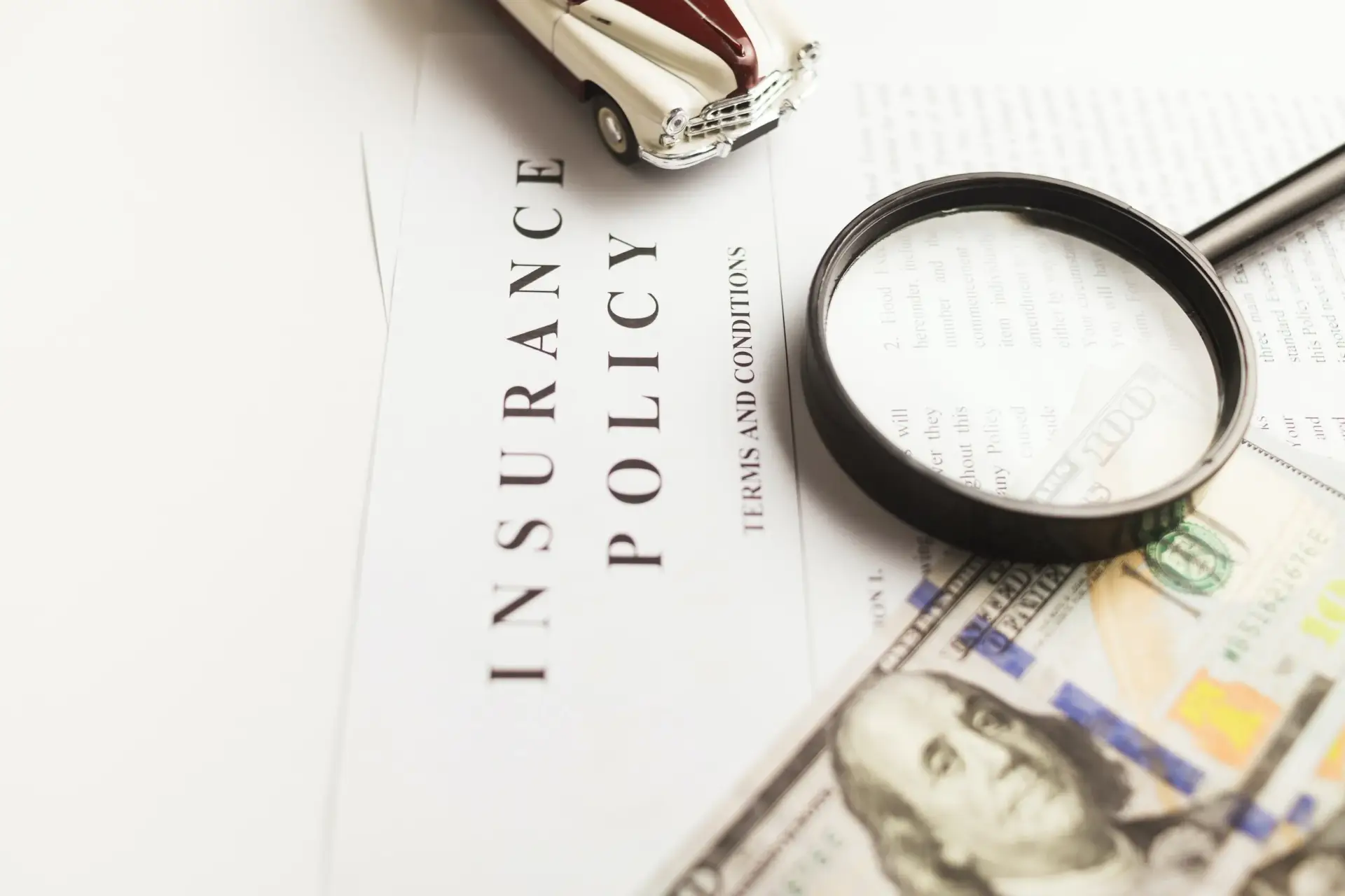 Insurance policy document with magnifying glass, cash, and toy car